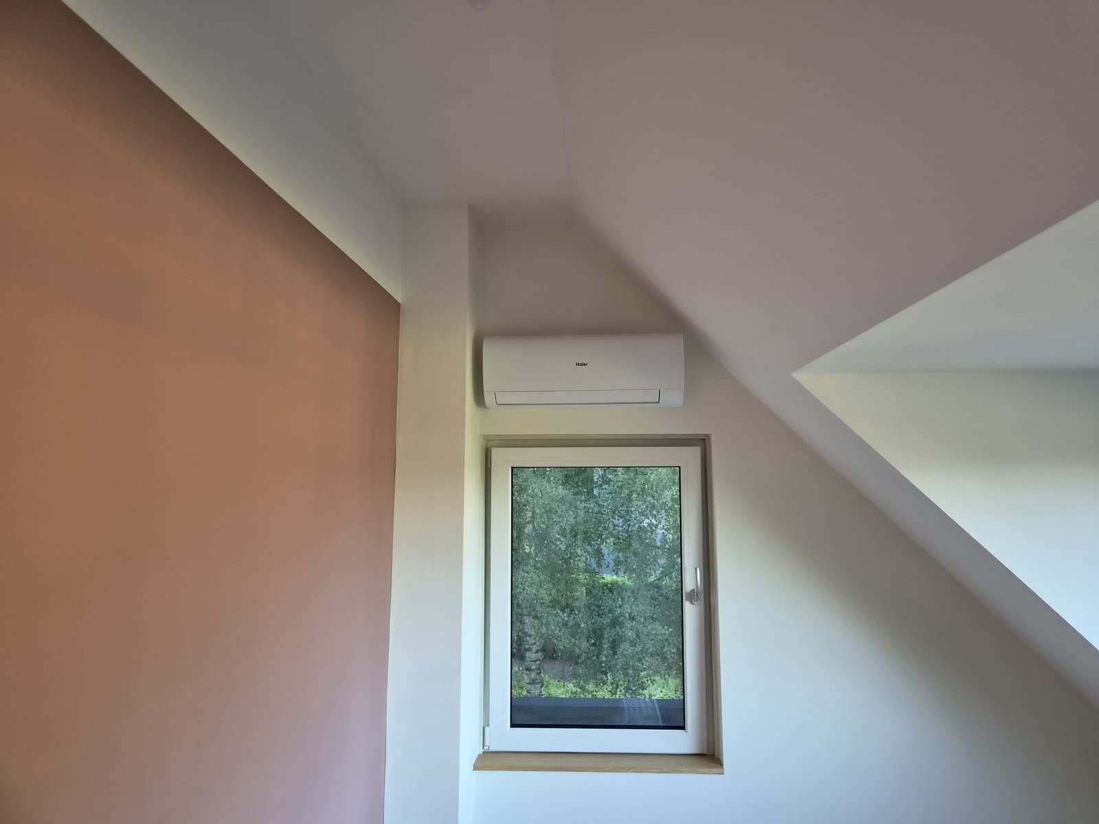 Haier airco binnenunit boven een raam bij een roze muur