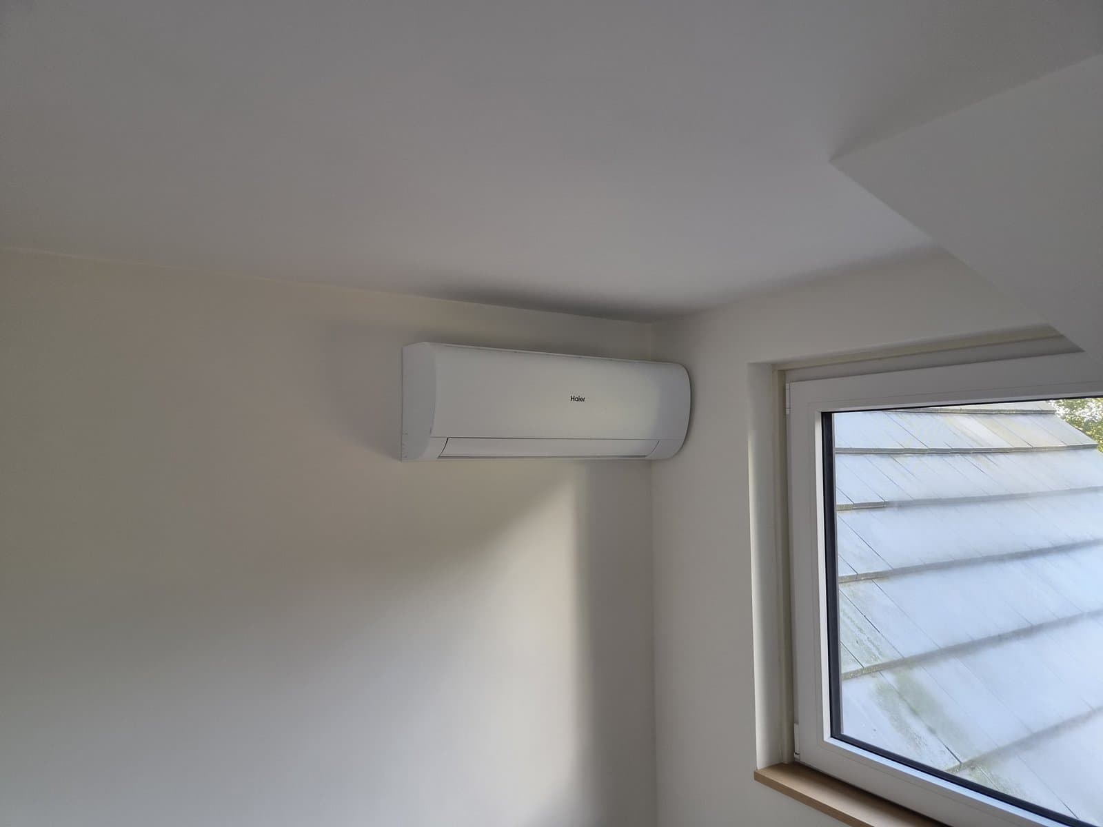 Witte Haier airco binnenunit netjes gemonteerd bij een dakraam